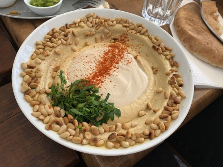 Bowl of hummus topped with herbs and pine nuts